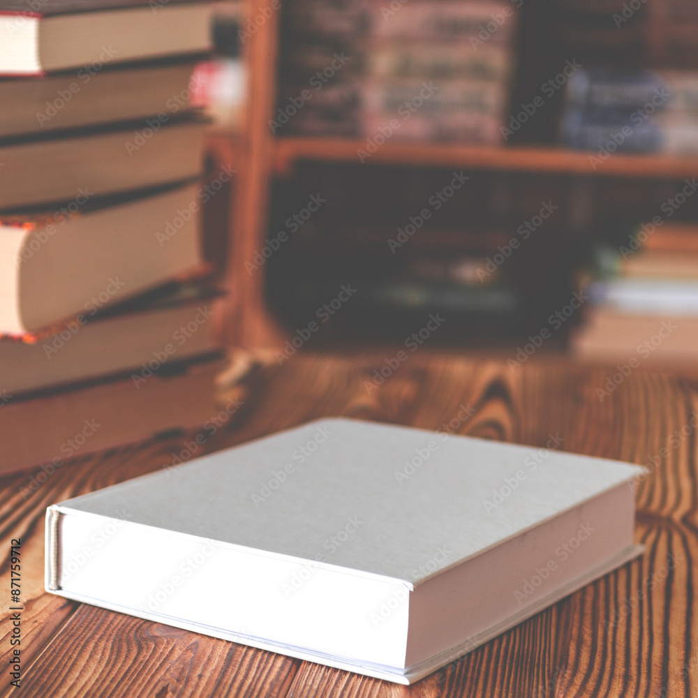 Books. A white notebook with space for text lies on a wooden table against the background of bookshelves