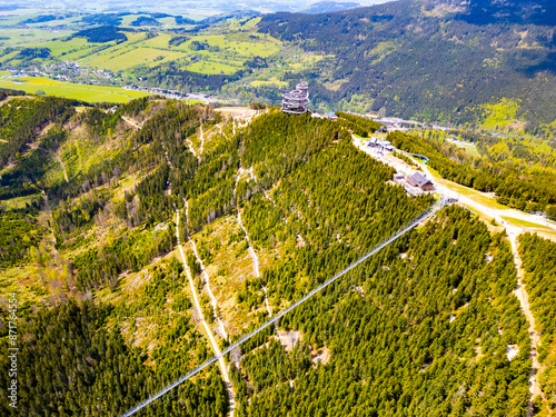 Aerial view of the Sky Bridge 721, the worlds longest suspension footbridge, stretching across a forested mountain in Czechia. The unique Sky Walk lookout tower stands nearby, offering panoramic views photo