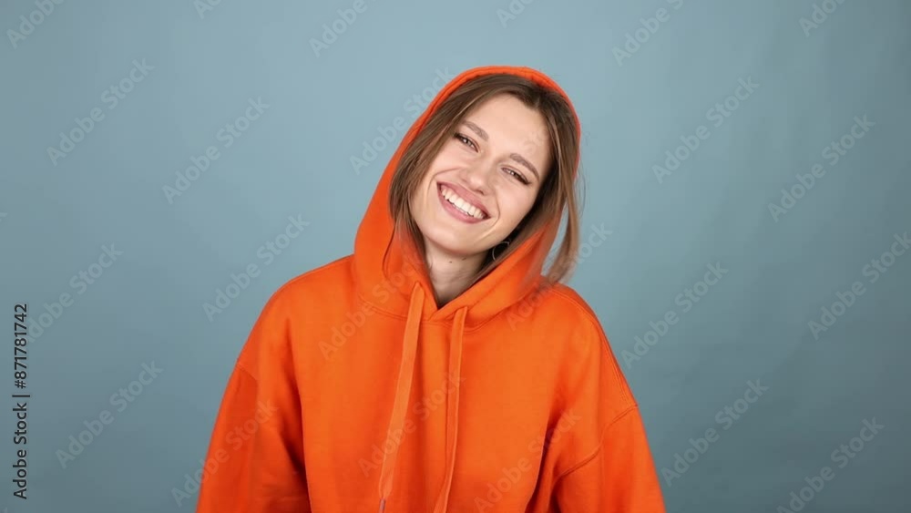 Woman Posing, Sad Face, Upset, Then Smiling, Wearing Orange Hoodie on Blue Background Slow Motion