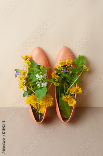 Orange peach fuzz shoes with spring bright and beauful flowers on beige background dandilion copy space top view