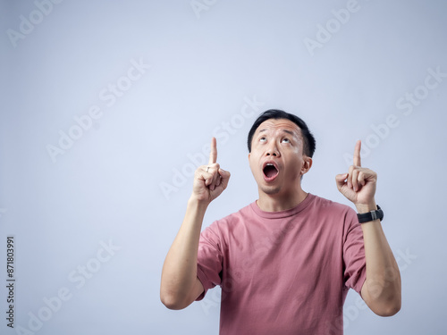 Εκτύπωση καμβά Asian man in a pink t-shirt, standing against a plain background, pointing upwar