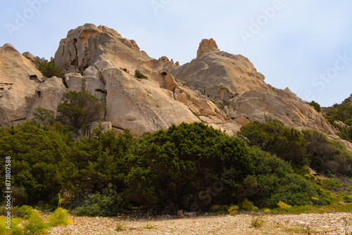 Formaciones rocosas en la isla de Caprera, parte del archipiélago de la Magdalena, Cerdeña, Italia. Grandes rocas de tonos beige y anaranjados se elevan sobre un denso follaje verde. photo