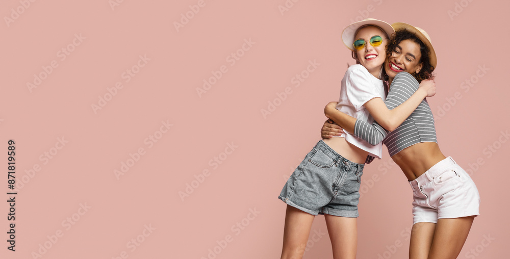 Two young women in summer outfits stand in front of a pink background. Both women have smiling expressions and are hugging each other, copy space Two young women in summer outfits stand in front of a pink background. Both women have smiling expressions and are hugging each other, copy space