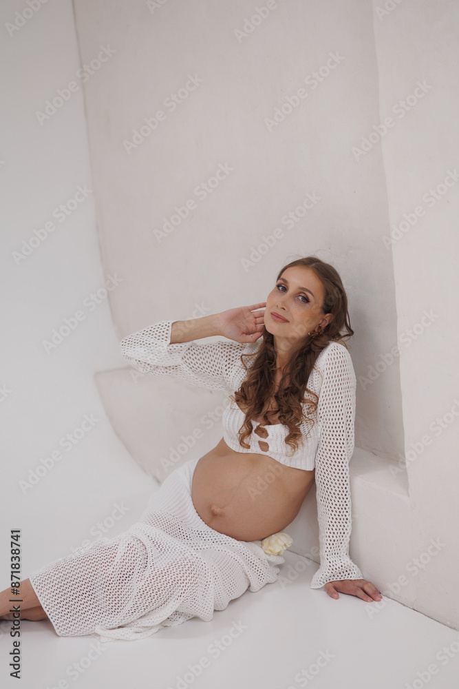 Beautiful pregnant woman in white separate dress. Big pregnant belly. Pretty woman waiting child. Light play on woman's body and face