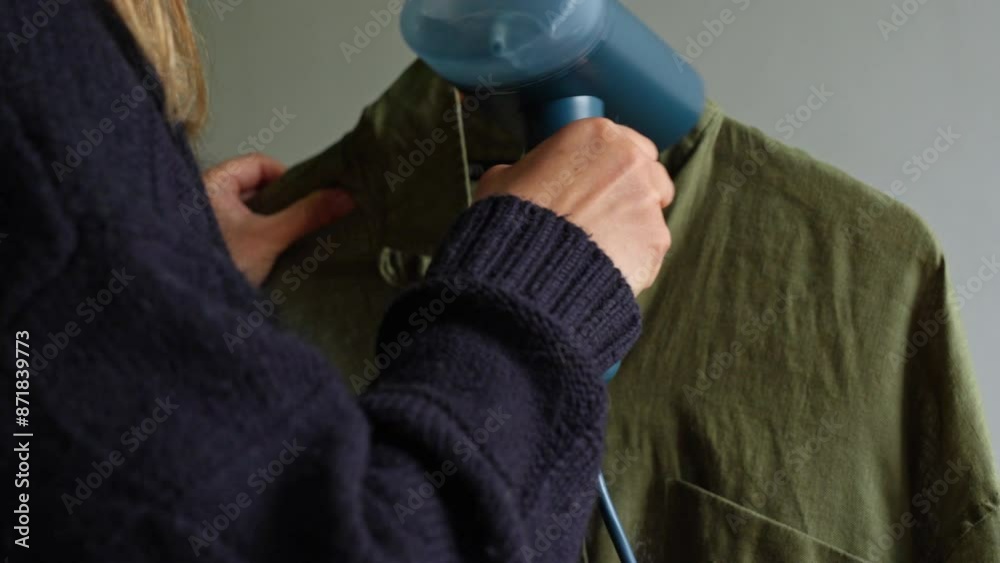 Close up of woman using electric hand steam generator while it is hot and steam comes out for clothes shirt at house Close up of woman using electric hand steam generator while it is hot and steam comes out for clothes shirt at house