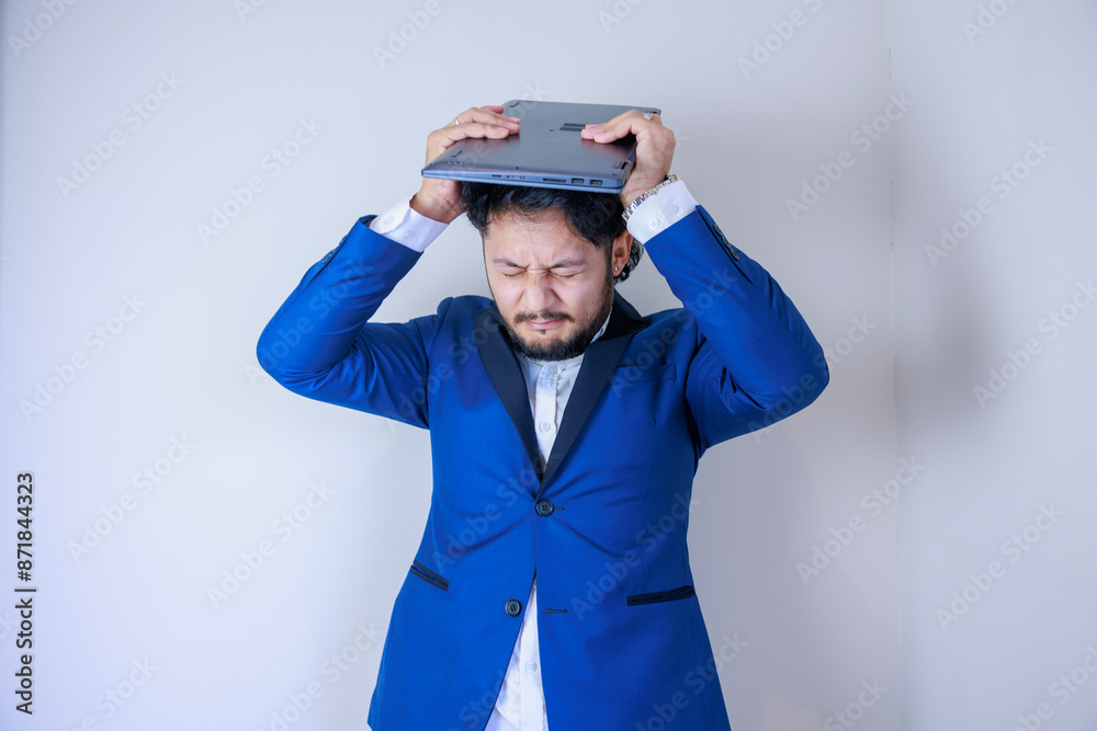 ノートパソコンを持ちながら頭を抱えるビジネスマン