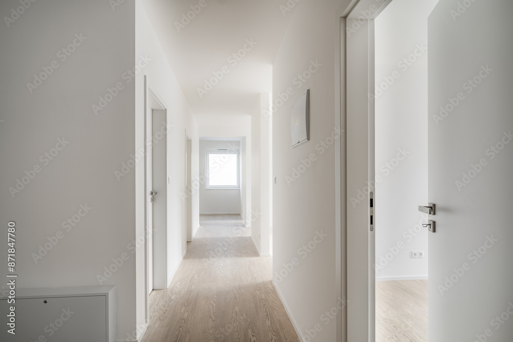 Minimalist, well-lit hallway in a modern apartment with wooden floors, white walls, and several doors leading to different rooms. Minimalist, well-lit hallway in a modern apartment with wooden floors, white walls, and several doors leading to different rooms.