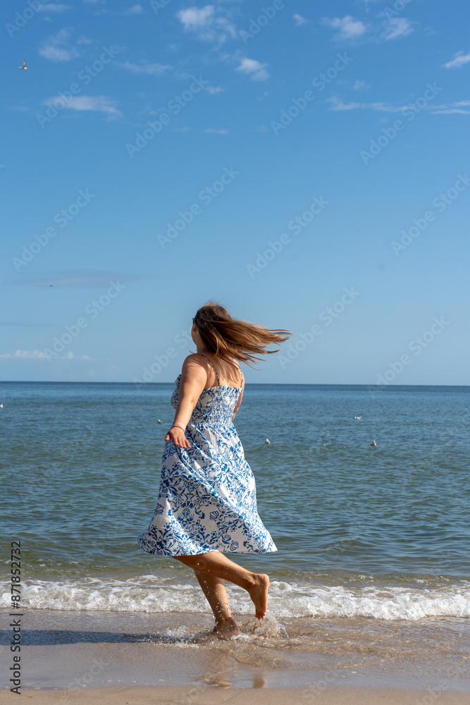 Woman in a dress running along the seashore on a sunny day. Concept of freedom and independence. Vertical photo. High quality photo Woman in a dress running along the seashore on a sunny day. Concept of freedom and independence. Vertical photo. High quality photo
