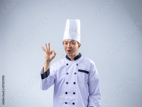 A cheerful Asian male chef in a white uniform and hat makes an 