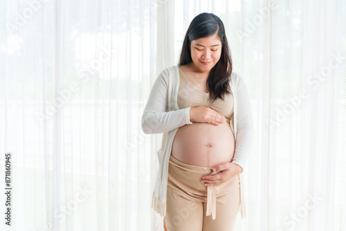 An Asian young pregnant wife relaxes at home, her hand gently resting on her belly, filled with love and anticipation as she embraces the journey of impending motherhood. Free Download An Asian young pregnant wife relaxes at home, her hand gently resting on her belly, filled with love and anticipation as she embraces the journey of impending motherhood. - GFXLoad