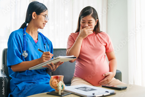 Asian female doctor and nurse consult on sofa with a pregnant woman, using ultrasound and stethoscope, addressing illnesses morning sickness, gestational diabetes, hypertension, ensuring her health. photo