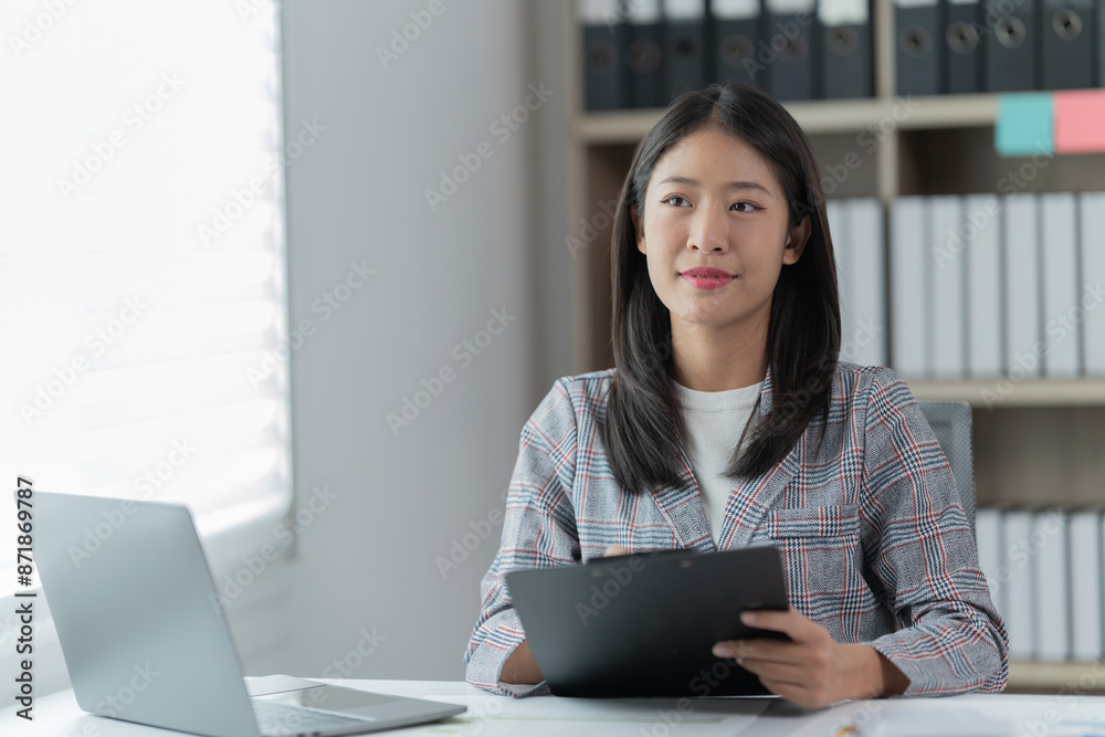 Sharing good business news. Attractive young businesswoman talking on the mobile phone and smiling while sitting at her working place in office and looking at laptop PC. Sharing good business news. Attractive young businesswoman talking on the mobile phone and smiling while sitting at her working place in office and looking at laptop PC.