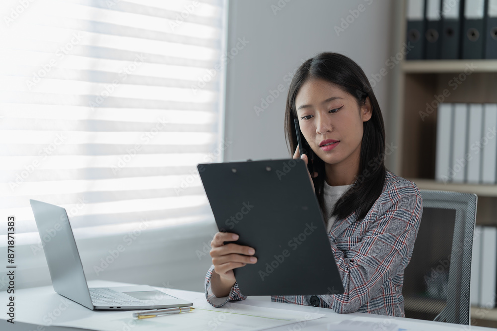 Sharing good business news. Attractive young businesswoman talking on the mobile phone and smiling while sitting at her working place in office and looking at laptop PC. Sharing good business news. Attractive young businesswoman talking on the mobile phone and smiling while sitting at her working place in office and looking at laptop PC.