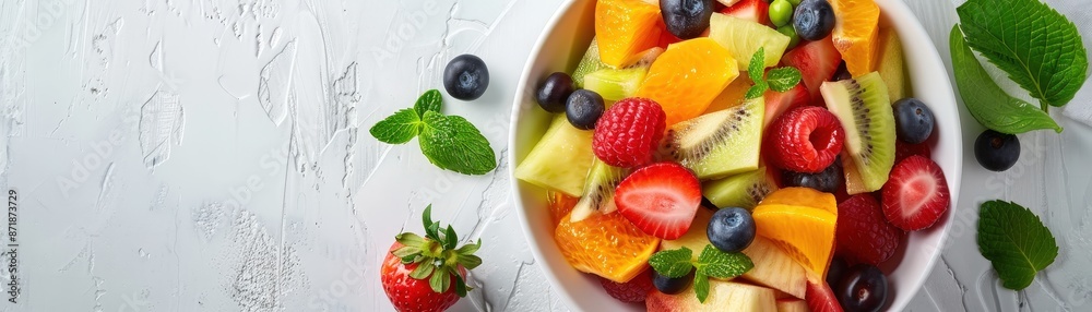 A colorful and healthy fruit salad featuring strawberries, kiwi, blueberries, and mint leaves in a white bowl on a textured white background. A colorful and healthy fruit salad featuring strawberries, kiwi, blueberries, and mint leaves in a white bowl on a textured white background.