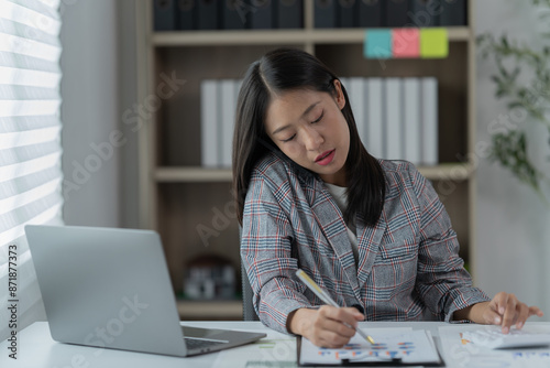 Sharing good business news. Attractive young businesswoman talking on the mobile phone and smiling while sitting at her working place in office and looking at laptop PC.