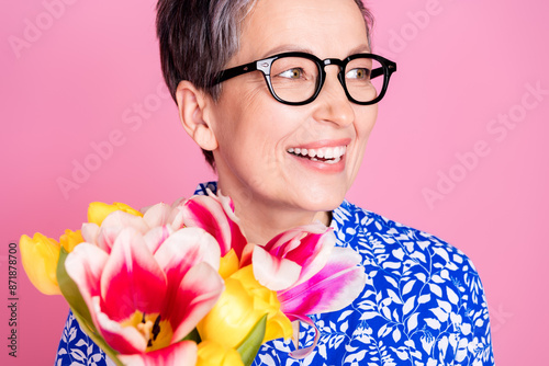 Photo of cheerful person with white gray hairstyle dressed print blouse hold tulips look empty space isolated on pink color background photo
