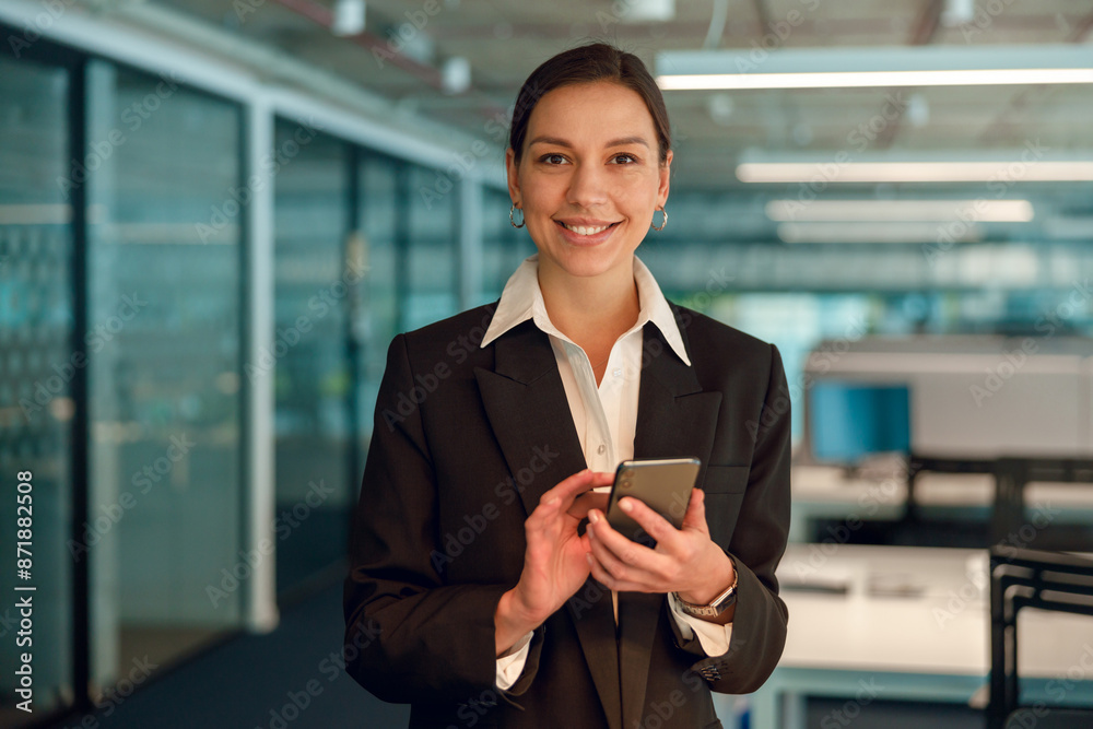 Businesswoman using smartphone in modern office, appearing confident and successful Businesswoman using smartphone in modern office, appearing confident and successful