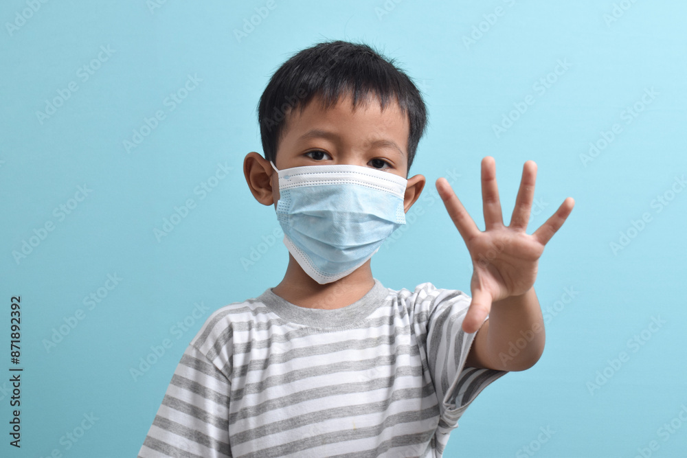 Asian Boy wearing health mask, showing palm with five fingers meaning don't or stop isolated on blue background. Medical and health concept Asian Boy wearing health mask, showing palm with five fingers meaning don't or stop isolated on blue background. Medical and health concept