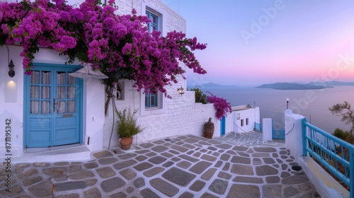 Fototapeta Naklejka Na Ścianę i Meble -  A picturesque Greek village street lined with whitewashed houses adorned with vibrant purple bougainvillea, overlooking a stunning sunset over the Aegean Sea