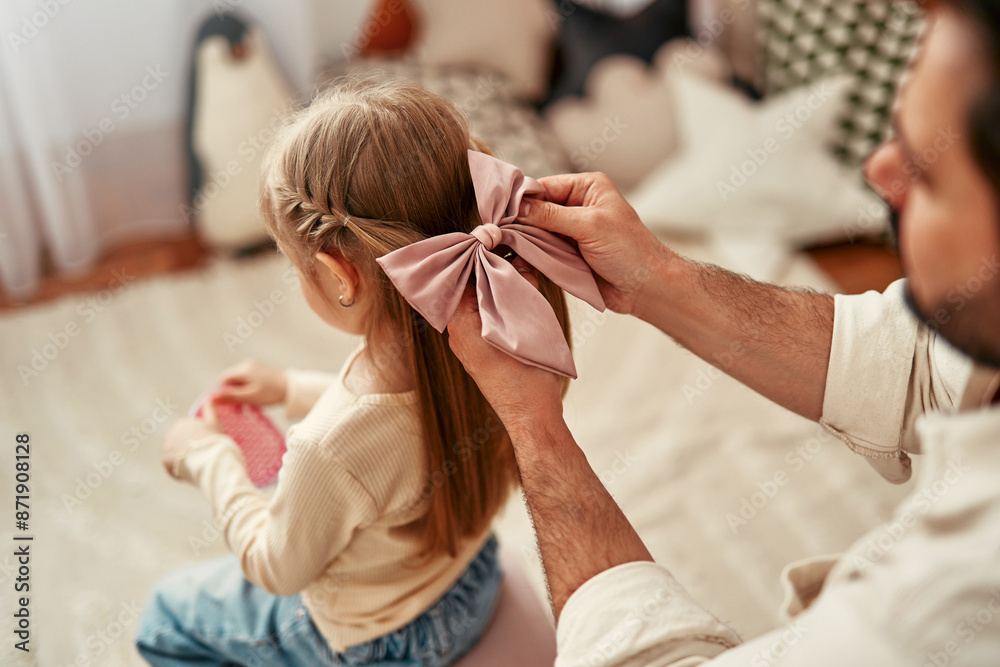 © Valerii Apetroaiei - A father ties a bow in his daughters hair, showing a strong bond and affectionate relationship