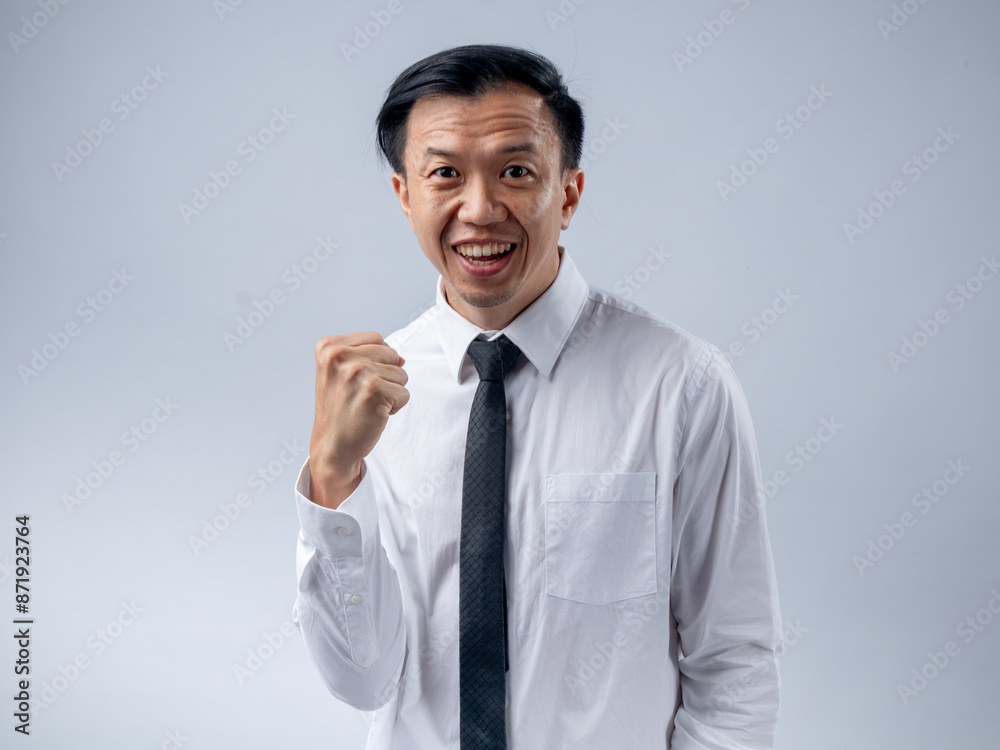 Asian businessman in white shirt and black tie celebrating success with fists clenched and mouth open in excitement, standing against a plain light background. His joyful expression and victory pose Asian businessman in white shirt and black tie celebrating success with fists clenched and mouth open in excitement, standing against a plain light background. His joyful expression and victory pose