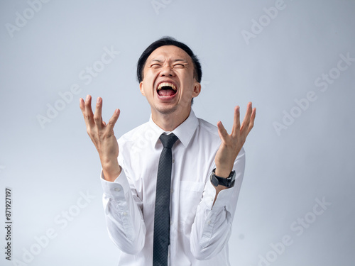 A cheerful Asian male in a white shirt and tie, with arms raised and laughing enthusiastically, conveys excitement and joy against a light blue background. The setting is professional and energetic.