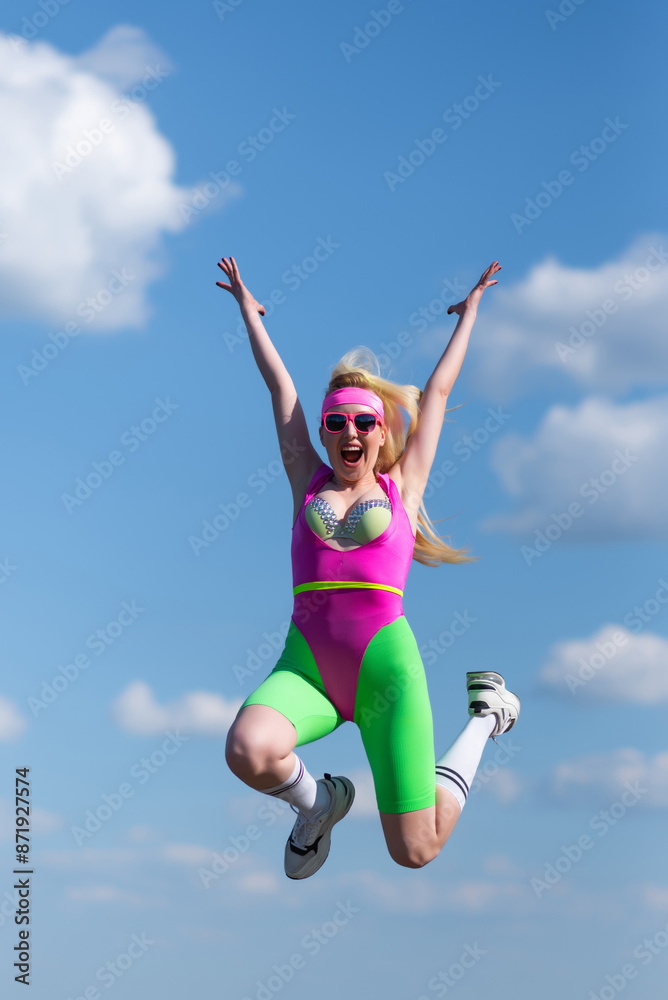 Young beautiful blonde woman in sports shorts, a pink bodysuit and pink sunglasses is doing sports outdoors. Jumping against the sky. Sports, Active lifestyle, sports training, healthy lifestyle Young beautiful blonde woman in sports shorts, a pink bodysuit and pink sunglasses is doing sports outdoors. Jumping against the sky. Sports, Active lifestyle, sports training, healthy lifestyle