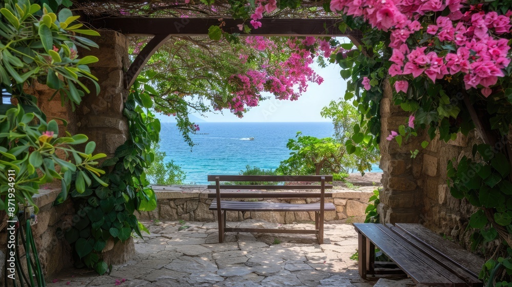 Obraz premium A wooden bench sits in the shade of a stone archway, overlooking the sparkling blue Mediterranean Sea. Pink flowers bloom profusely from a vine growing on the archway