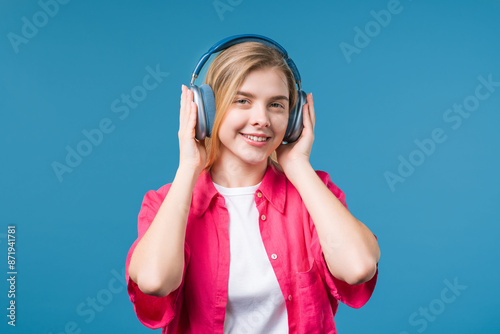 Cute woman listening streaming music, enjoying dance with headphones on blue