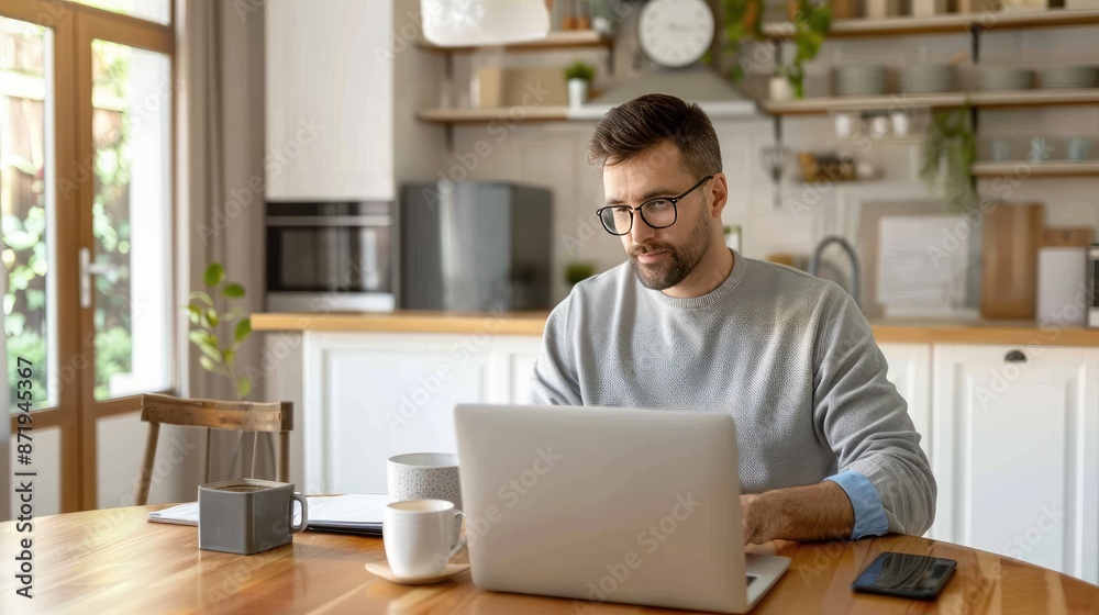 A man sits at a table in his home office, working on a laptop computer A man sits at a table in his home office, working on a laptop computer