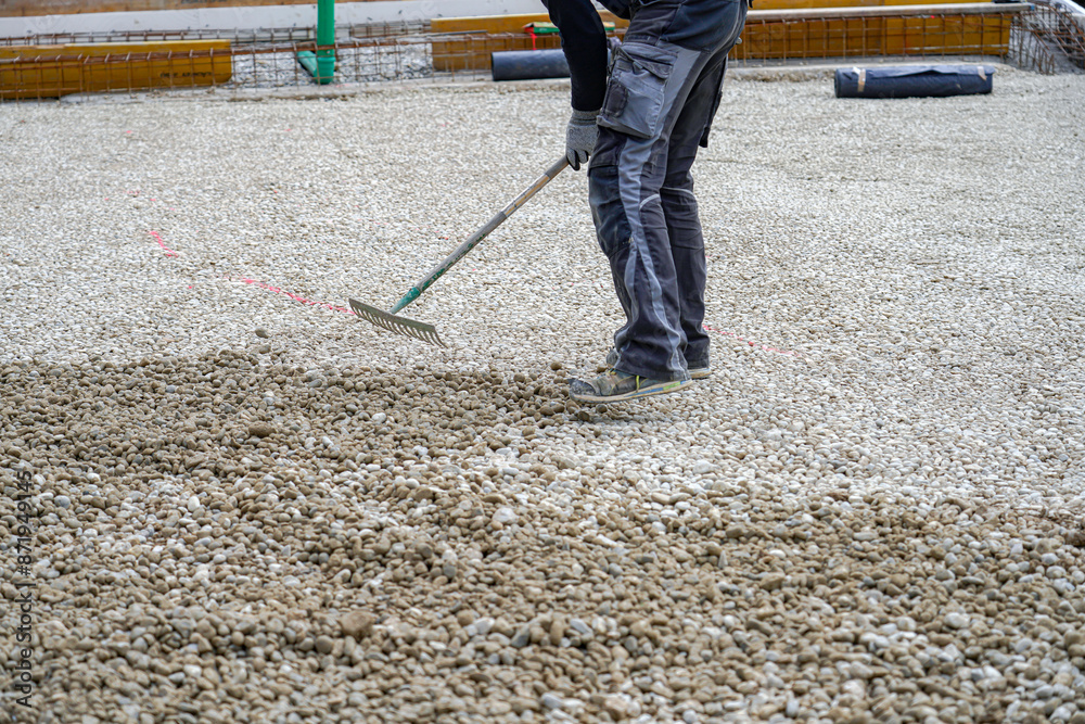A worker uses a rake to level crushed stone before pouring concrete. A worker uses a rake to level crushed stone before pouring concrete.