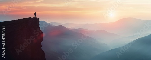A lone figure silhouetted on a cliff, overlooking a mountain range at dawn.