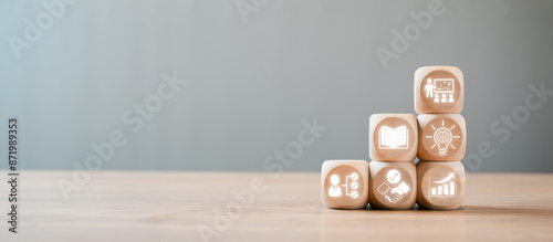 Wooden blocks with icons symbolizing capacity building, education, growth, and development on a wooden table against a neutral background.