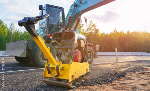 Ground Compactor Plate on compact soil. Plate Compactor for Ground compact on construction site. Vibratory plate on compacting beating sand at sidewalk. Pressing gravel for laying paving slabs photo