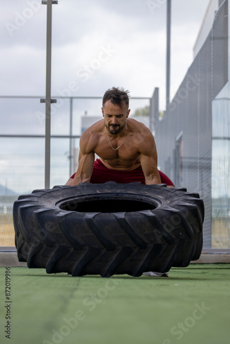 Strong shirtless man lifting a truck wheel.
