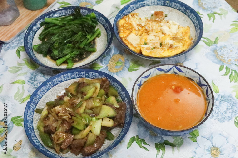 close up top shot of homemade Cantonese Hong Kong style household food with fried egg and tofu, boiled choy sum vegetables, tomato vegetable soup and stir fried celery with beef in blue plates close up top shot of homemade Cantonese Hong Kong style household food with fried egg and tofu, boiled choy sum vegetables, tomato vegetable soup and stir fried celery with beef in blue plates