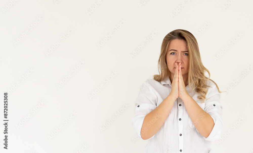 Portrait of imploring girl tilts head, purses lips, looks sadly at camera, makes praying gesture, asks for help and support, begs boyfriend for apologize, wears blue t-shirt, isolated on white wall Portrait of imploring girl tilts head, purses lips, looks sadly at camera, makes praying gesture, asks for help and support, begs boyfriend for apologize, wears blue t-shirt, isolated on white wall