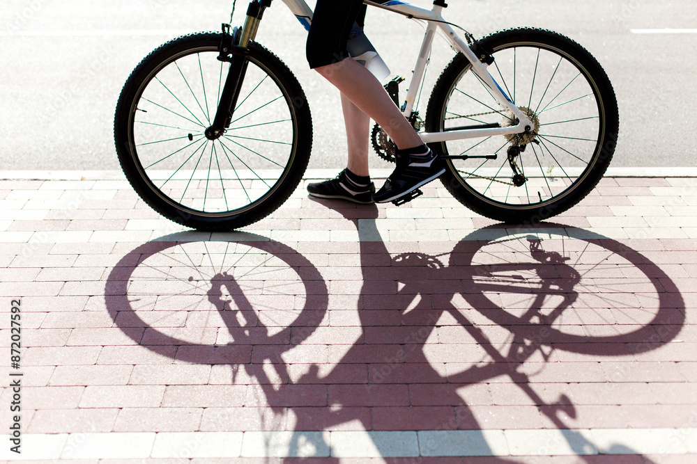 Woman riding bike on city street. Urban road with bicycle path. Close up of cyclists legs, wheels and shadows. Sport outdoor activity. Healthy and sustainable lifestyle. Ecological transportation Woman riding bike on city street. Urban road with bicycle path. Close up of cyclists legs, wheels and shadows. Sport outdoor activity. Healthy and sustainable lifestyle. Ecological transportation