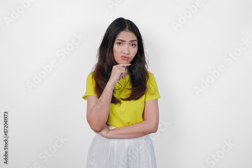 Thoughtful young Asian woman in a yellow shirt and white skirt is looking down and appears to be thinking. Concept of introspection and contemplation.