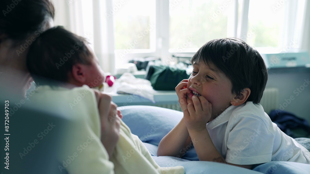 Obraz premium Young boy gazing at newborn sibling in mother's arms with awe and curiosity in a bright hospital room. moment captures the wonder and excitement of meeting a new family member for the first time