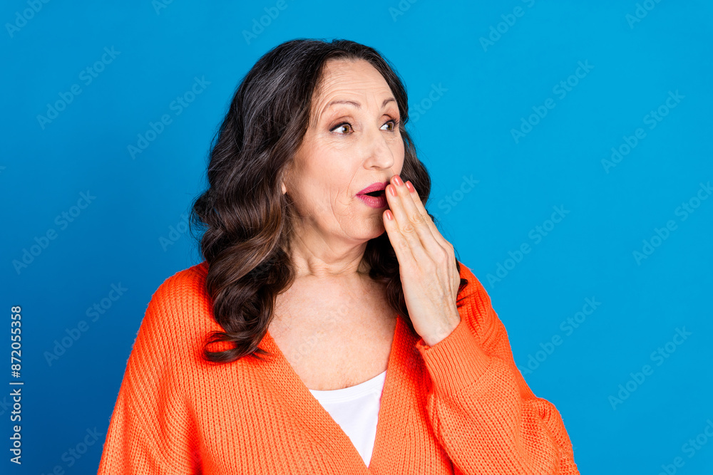 Photo of attractive senior woman cover mouth amazed look empty space dressed stylish orange clothes isolated on blue color background Photo of attractive senior woman cover mouth amazed look empty space dressed stylish orange clothes isolated on blue color background