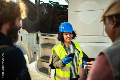 Female logistics manager with clipboard discussing with truck drivers