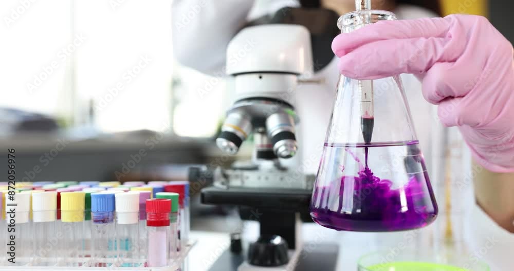 Scientist holds transparent flask with liquid and digs into it purple toxin reagent. Chemical research in laboratory concept