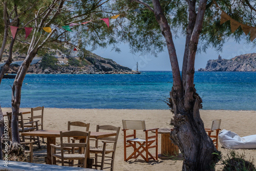 View of a beach bar’s tables and chairs next to a tree at the Gialos Beach in Ios Greece