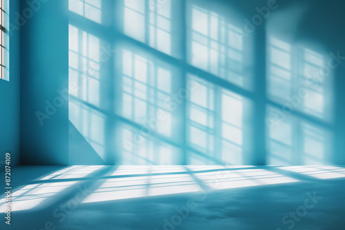 Interior of empty spacious room with window shadows and sunlight on blue wall.