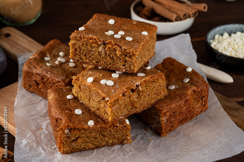 Pumpkin brown butter blondies or pumpkin cake with white chocolate drops and spices on a dark wooden background. Dessert for Thanksgiving or Halloween.