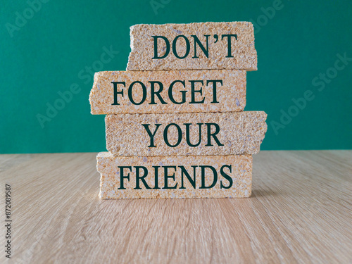 Remembering friends and friendship concept. The message Don't Forget Your Friends on brick blocks. Beautiful green background, wooden table.