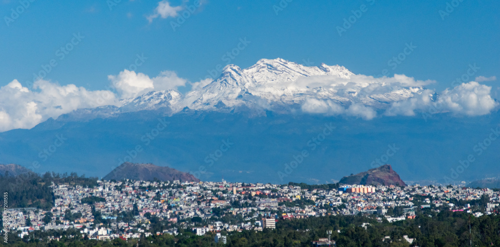 Obraz premium A mesmerizing view of Iztaccíhuatl, the majestic snow-capped volcano, towering over the bustling cityscape below.