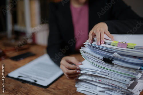 Businesswoman organizing a large stack of documents on the desk. Office work, paperwork, and administration concept.