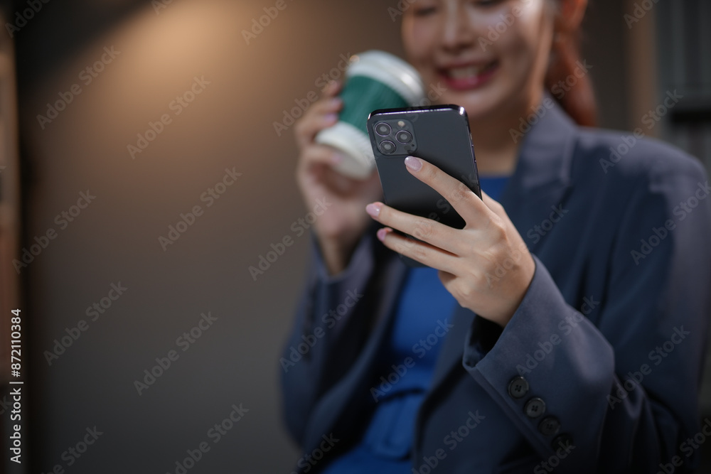 Businesswoman smiling, holding coffee and using smartphone in modern office setting. Relaxed, professional attire and environment. Businesswoman smiling, holding coffee and using smartphone in modern office setting. Relaxed, professional attire and environment.